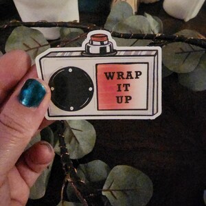 May include: A white and black cassette tape with a red button and a red and white label that says "WRAP IT UP".