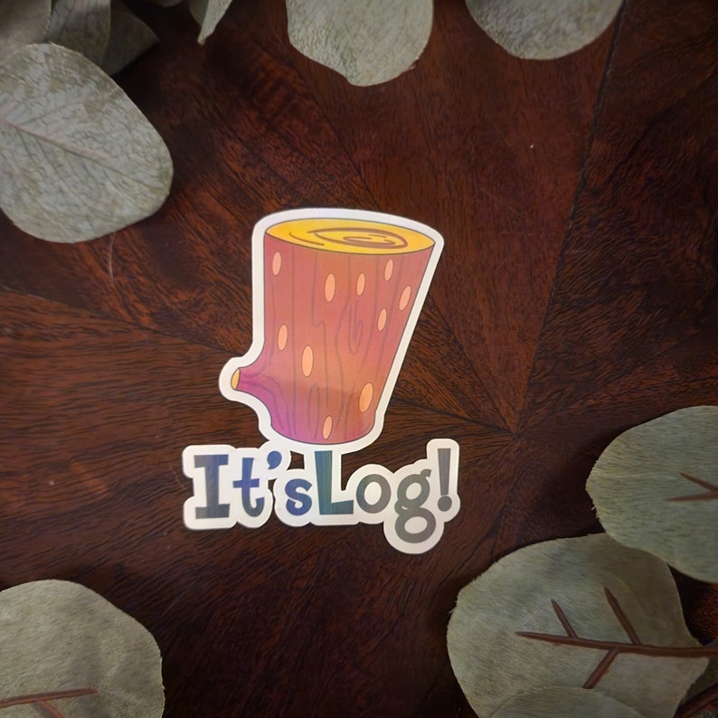 Pu&ograve; includere: Un adesivo raffigurante un tronco di cartone animato nei toni del giallo, arancione e viola, con la scritta "It's Log!". L'adesivo &egrave; posto su uno sfondo di legno scuro, incorniciato da foglie verdi.