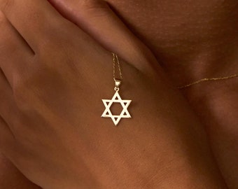Puede incluir: Un collar de cadena de oro con un colgante de Estrella de David. El colgante es un diseño simple y geométrico.