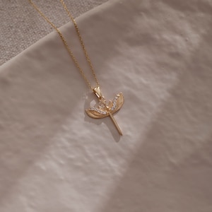 May include: A gold necklace with a pendant featuring a sword with wings and clear crystals.