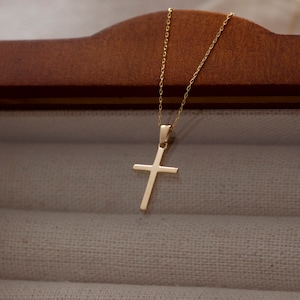 May include: A gold chain necklace with a simple gold cross pendant.