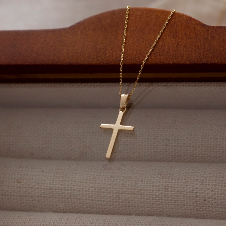 May include: A gold chain necklace with a simple gold cross pendant.
