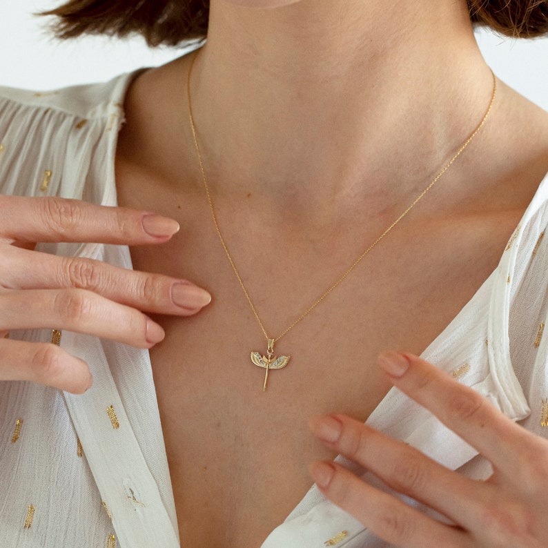 May include: A gold chain necklace with a delicate pendant featuring a stylized dragonfly design with clear gemstones.