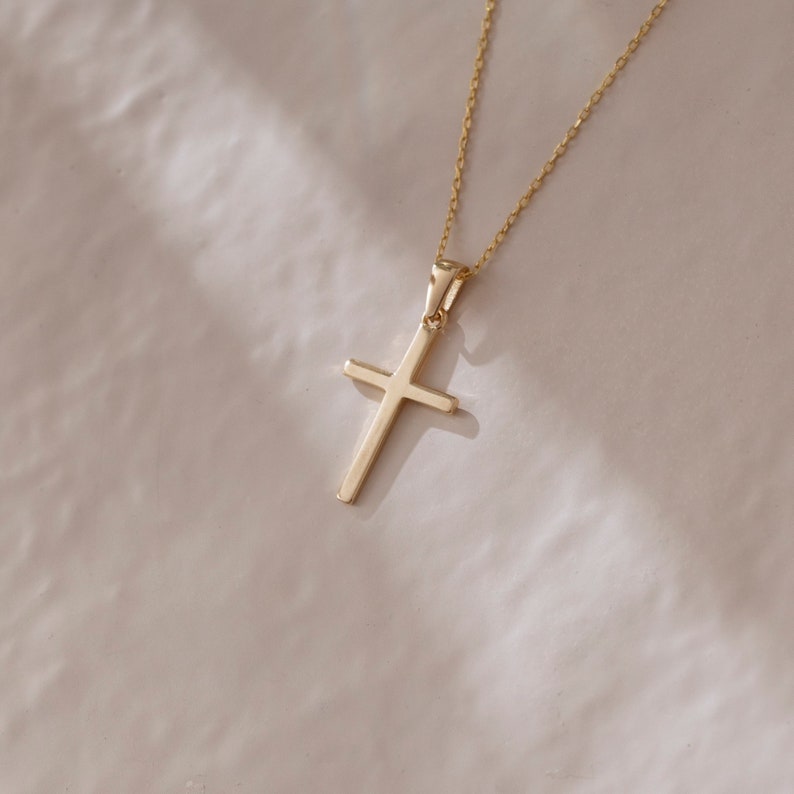May include: A gold chain necklace with a simple gold cross pendant.