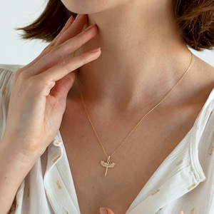 May include: A gold chain necklace with a delicate pendant featuring a stylized winged sword design. The pendant has small clear stones set into the wings.