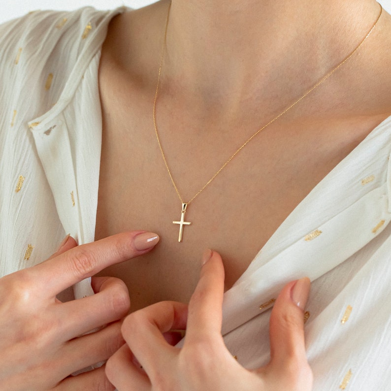 May include: A gold chain necklace with a small, simple gold cross pendant.