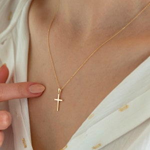 May include: A gold chain necklace with a small, simple gold cross pendant.