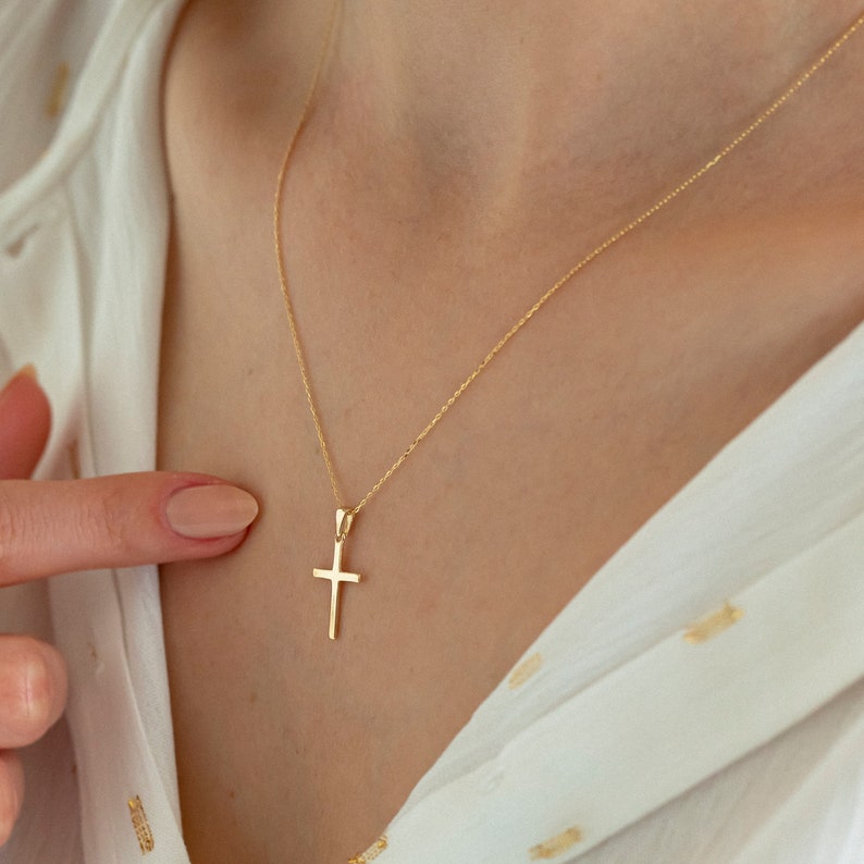 May include: A gold chain necklace with a small, simple gold cross pendant.