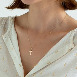 May include: A gold chain necklace with a small, simple gold cross pendant.