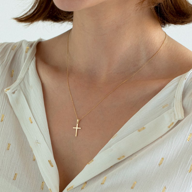May include: A gold chain necklace with a small, simple gold cross pendant.