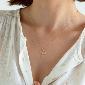 May include: A gold chain necklace with a dragonfly pendant. The dragonfly is detailed with small, clear stones.