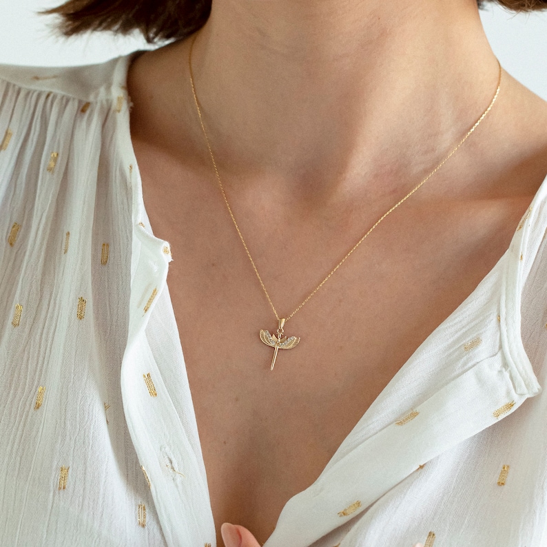 May include: A gold chain necklace with a dragonfly pendant. The dragonfly is detailed with small, clear stones.