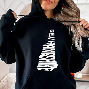 May include: Black hooded sweatshirt with a white graphic of the state of New Hampshire, with the state name spelled out within the outline of the state.