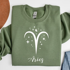 May include: A green sweatshirt with a white Aries zodiac sign and stars. The text "Aries" is written below the sign.