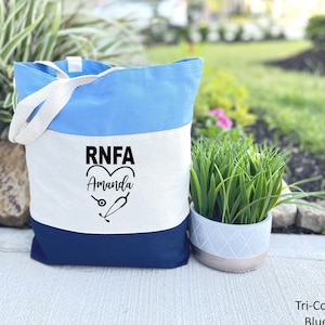 May include: A blue, white, and navy blue canvas tote bag with the text "RNFA Amanda" and a stethoscope and heart graphic.