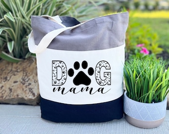 May include: A tri-color tote bag with a white panel featuring the text "DOG mama" in black with a paw print in the center. The bag is grey, white, and black.
