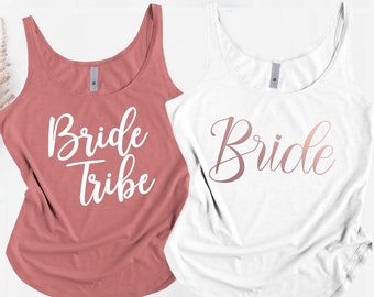 May include: Two tank tops, one white and one paprika red, with the word "Bride" in a cursive font. The red tank top says "Bride Tribe" in white text.