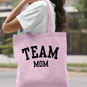 May include: Light pink canvas tote bag with black text that reads "TEAM MOM".