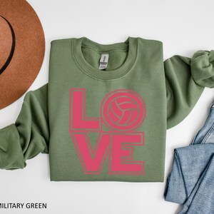 May include: A green sweatshirt with the word "LOVE" in pink letters, with a volleyball graphic in the "O".