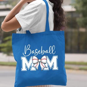 May include: A royal blue tote bag with white text that reads "Baseball Mom" and a white baseball-themed bow with red stitching.
