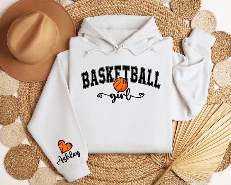 May include: White hoodie with a black basketball graphic and the text "Basketball girl" with a heart. The sleeve has a heart with a basketball graphic and the text "Ashley".