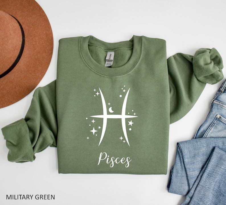 Op de afbeelding: Een groen sweatshirt met een wit Vissen-sterrenbeeld en het woord "Vissen" gedrukt op de voorkant.