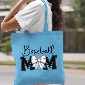 May include: Light blue tote bag with the text "Baseball Mom" in black lettering. A white and red baseball-themed bow is centered between the "M"s.
