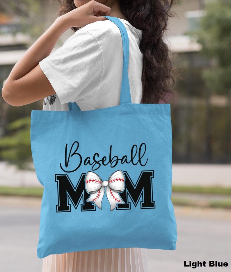 May include: Light blue tote bag with the text "Baseball Mom" in black lettering. A white and red baseball-themed bow is centered between the "M"s.