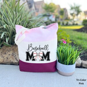 May include: A pink and burgundy tote bag with the text "Baseball Mom" in black letters and a white baseball with a red bow on top.