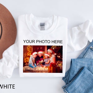 May include: White sweatshirt with a photo of a family of four wearing Santa hats and holding a book in front of a Christmas tree. The text "YOUR PHOTO HERE" is printed above the photo.