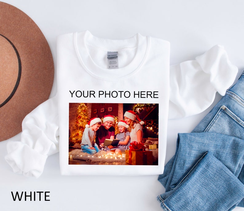 May include: White sweatshirt with a photo of a family of four wearing Santa hats and holding a book in front of a Christmas tree. The text "YOUR PHOTO HERE" is printed above the photo.