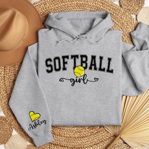 May include: Gray softball hoodie with the text "Softball girl" and a softball graphic. The left sleeve has a heart with the name "Ashley" on it.