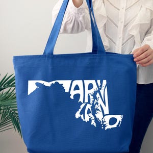 May include: A blue tote bag with white text and a graphic of the state of Maryland. The bag has two blue handles and is made of a sturdy fabric. The text on the bag reads "MARYLAND".