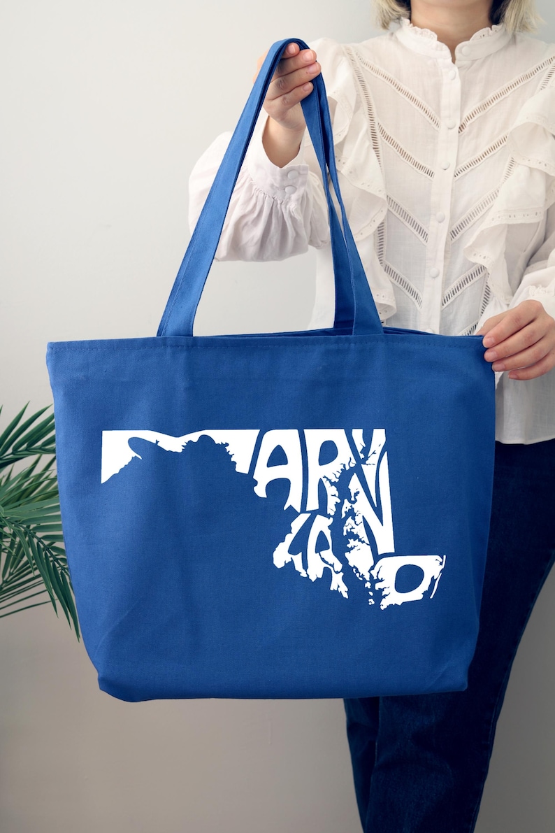 May include: A blue tote bag with white text and a graphic of the state of Maryland. The bag has two blue handles and is made of a sturdy fabric. The text on the bag reads "MARYLAND".