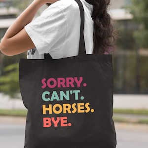 K&ouml;nnte beinhalten: Schwarze Einkaufstasche mit dem Text "SORRY. CAN'T. HORSES. BYE." in bunten Buchstaben.