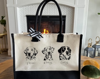 May include: A canvas tote bag with black trim and handles. The bag features three dog portraits with the names "Max", "Roxy", and "Lucy" below each image. A black and white striped bow is attached to the top of the bag.