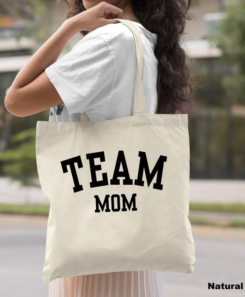 May include: A natural canvas tote bag with black text that reads "TEAM MOM".