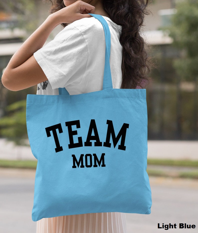 May include: Light blue tote bag with black text that reads "TEAM MOM".