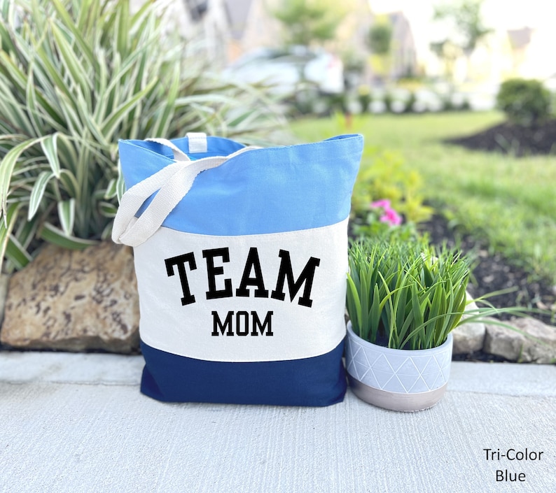 May include: A blue, white, and navy blue canvas tote bag with the text "TEAM MOM" in black.