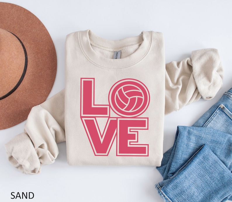 May include: A beige sweatshirt with the word "LOVE" in pink letters with a volleyball graphic in the "O".