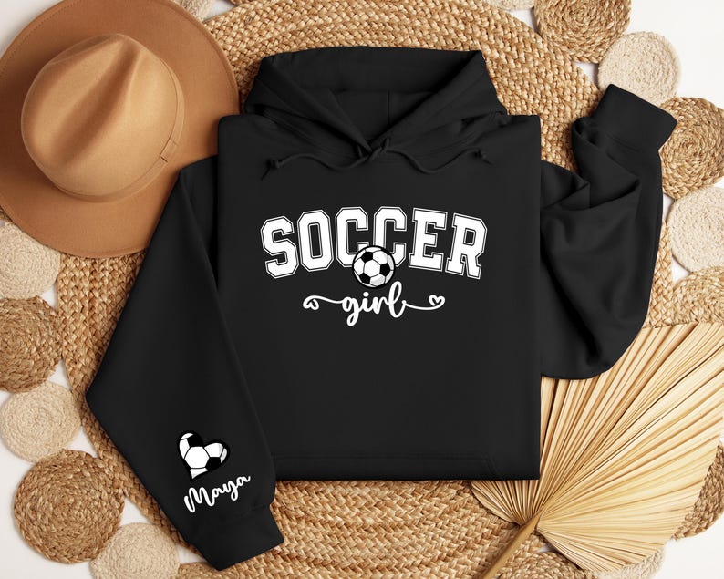May include: Black hoodie with a white graphic that says "Soccer girl" with a soccer ball and a heart. The left sleeve has a white heart with a soccer ball and the name "Maya" written below.