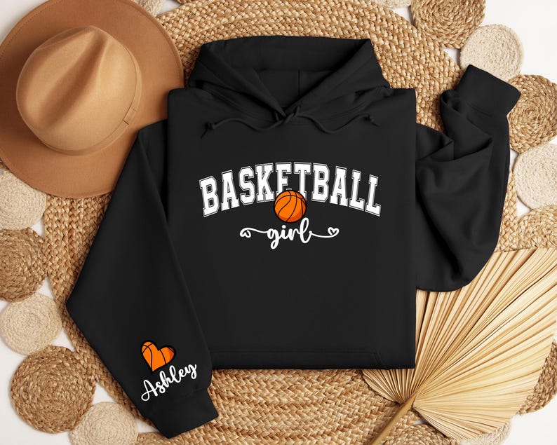 May include: Black hooded sweatshirt with the text "Basketball girl" and a basketball graphic. The sleeve has a heart with the name "Ashley" on it.
