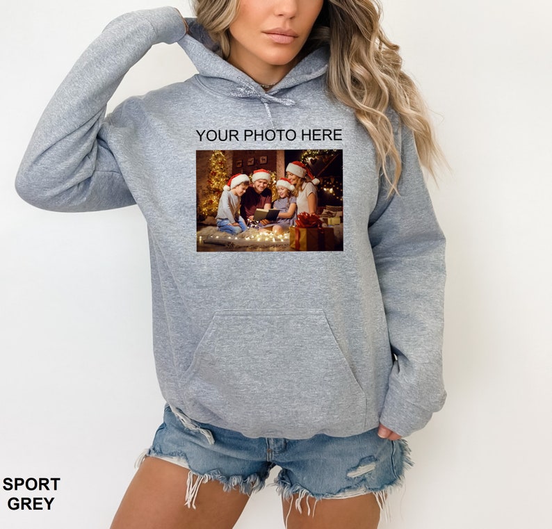 May include: A gray hooded sweatshirt with a pocket on the front. The sweatshirt has a photo printed on the front of a family in Christmas hats sitting around a Christmas tree. The text "YOUR PHOTO HERE" is printed above the photo.