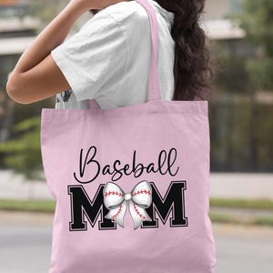 May include: Light pink tote bag with black text that reads "Baseball Mom" and a white baseball-themed bow.