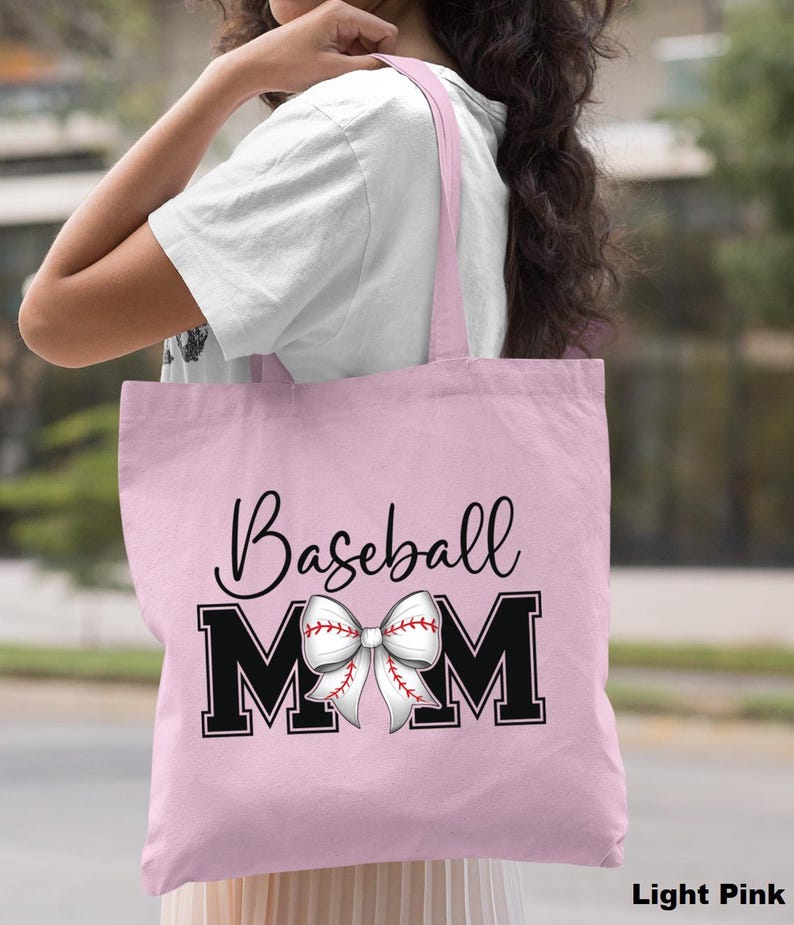 May include: Light pink tote bag with black text that reads "Baseball Mom" and a white baseball-themed bow.