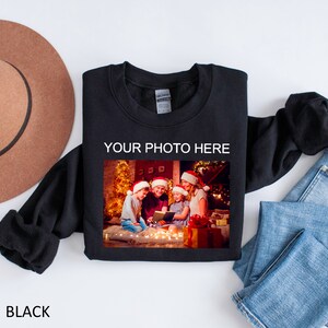 May include: Black sweatshirt with a photo of a family in front of a Christmas tree. The text "YOUR PHOTO HERE" is printed above the photo.