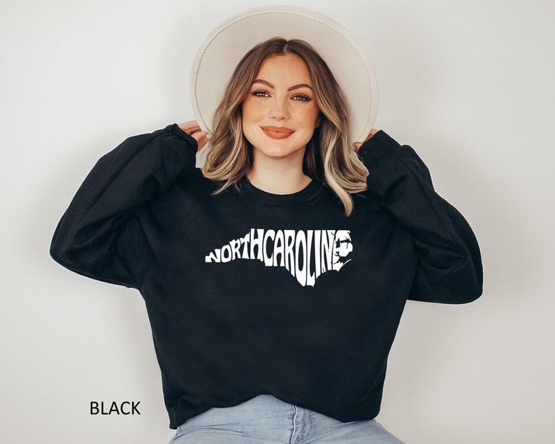 K&ouml;nnte beinhalten: Ein schwarzer Pullover mit einem wei&szlig;en Aufdruck des Bundesstaates North Carolina, wobei das Wort "NORTH CAROLINA" in Form des Bundesstaates ausgeschrieben ist.