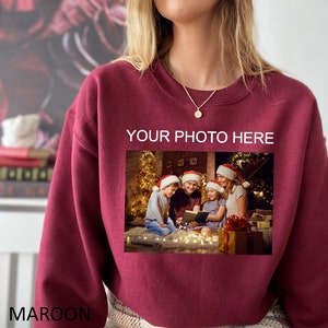 May include: Maroon sweatshirt with a photo of a family in front of a Christmas tree. The text "YOUR PHOTO HERE" is printed on the sweatshirt.