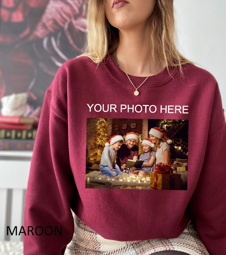 May include: Maroon sweatshirt with a photo of a family in front of a Christmas tree. The text "YOUR PHOTO HERE" is printed on the sweatshirt.