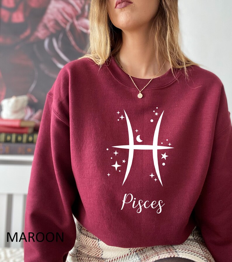 Op de afbeelding: Een bordeauxrood sweatshirt met een wit Vissen-sterrenbeeld en het woord "Vissen" gedrukt op de voorkant.
